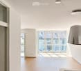 Bright, minimalist room with light wooden flooring, white walls, large windows, and a modern pendant light fixture.