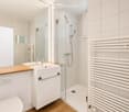 Modern bathroom with white tiles, a glass-enclosed shower, a sink with a wooden countertop, a toilet, and a white radiator.