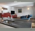 Modern living room with a blue sofa, red cabinet, television, and a kitchen area featuring a sink and faucet.