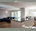 Open-plan living and kitchen area with a dark blue sofa, kitchen island, and modern fixtures.