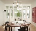 Spacious dining room with large windows overlooking a balcony or terrace, wooden oval dining table, black chairs, and a decorative chandelier above the table.