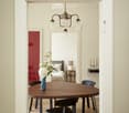 Dining room with a round wooden table, black chairs, a chandelier, and a fireplace visible in the background.