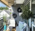 Balcony with a grey sofa, blue and white patterned cushions, a small table with a blue vase, and a potted olive tree.