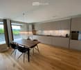 Modern kitchen with light wood flooring, a wooden dining table with four black chairs, a chandelier, and built-in cabinets.