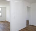 Empty room with white walls, wooden flooring, and a window with a view of the outside. No furniture or equipment is present.