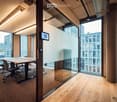 Modern office space with large glass windows, a wooden table, and chairs, featuring a sleek design and natural light.