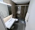 Modern bathroom with a white sink, toilet, glass-enclosed shower, and large mirror. Towels are neatly hung on both sides of the mirror, and a small rug is placed in front of the shower.
