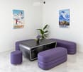 Modern lounge area with white walls, marble flooring, purple seating, and a black table with a flower vase.