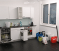 Modern kitchen with white cabinets, black countertops, and stainless steel appliances. Features a dishwasher, oven, sink, and various items including a backpack and handbags.