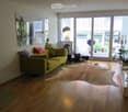 Bright living room with large windows and a balcony, featuring a green sofa, coffee table, floor lamp, and decorative mirror.