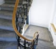 Spiral staircase with wooden handrails and black metal balustrade, leading to an upper level.