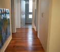 A long, well-lit hallway with wooden flooring, white walls, and a door at the end leading to another room.