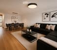 Modern living room with a black sectional sofa, coffee table, dining area with chairs, pendant lights, and artwork on the walls.