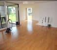 Empty room with wooden flooring, large sliding glass doors leading to a balcony, and a vacuum cleaner placed near the entrance.