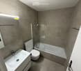 modern bathroom with white bathtub, white toilet, white sink, gray tiles, glass shower enclosure
