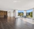 An empty, modern living space with large glass sliding doors leading to an outdoor area, polished dark tile flooring, and a textured stone accent wall.