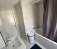 Modern bathroom with a white sink, bathtub, showerhead, and a dark blue bath mat on the floor.