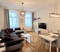 Modern living and dining area with a grey sectional sofa, coffee table, dining table with chairs, wall-mounted TV, and decorative items including candles and a picture frame.