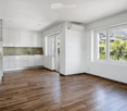 Empty room with white walls, wooden flooring, white cabinets, and large windows offering a scenic view.