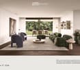Modern living room with a large green sectional sofa, a round coffee table, armchairs, ottoman, floor lamp, dining area with chairs and table, shelves, plants, and artwork.