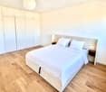 Modern bedroom with a large double bed, white bedding, wooden flooring, built-in wardrobes, and bedside tables.
