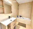 Modern bathroom with a white sink, black faucet, wooden cabinet, bathtub, mirror, and a small rug on the floor.