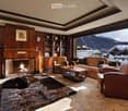 Elegant living room with a fireplace, leather sofa, armchairs, coffee table, bookshelf, and a scenic mountain view through large windows.