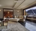 Elegant living room with patterned wallpaper, large window showcasing a snowy mountain view, a patterned sofa, ottoman, armchair, coffee table, fireplace, and a mirror.