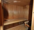 Wooden sauna with multiple wooden benches and a small control panel on the wall.