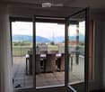 Balcony with a view of a green field and mountains, featuring a dining table and chairs.