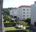 View from a balcony overlooking a landscaped garden area with trimmed hedges, small trees, and a pathway leading to a modern residential building complex.