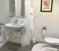 Modern bathroom with white tiles, a sink, mirror, toilet, bidet, bathtub, and various toiletries.