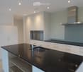 Modern kitchen with white cabinets, black countertops, stainless steel sink and faucet, built-in oven, and range hood.