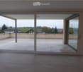 Empty room with tiled floor and large sliding glass doors opening to a tiled balcony with a view of the countryside.