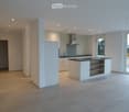 Modern kitchen with white cabinets, a central island, and a black countertop. Features include a range hood, sink, and large windows providing natural light.