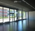 Empty, modern interior space with large glass windows and polished dark flooring. Minimalist design with no furniture or equipment visible.