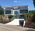 Modern two-story house with white exterior, large windows, multiple balconies, and a garage entrance.