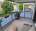 Balcony with a small seating area, a table, a grill, and potted plants.
