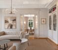 Elegant living room with a cream-colored sofa, coffee table, armchairs, dining area, bookshelf, and artwork.