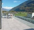 Balcony with a table and chairs, overlooking a scenic mountain landscape and green fields.