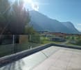 A modern balcony with a glass railing, tiled floor, and scenic mountain view.
