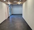 Empty hallway with dark tiled floor, light-colored walls, wooden ceiling, and recessed lighting. Features a door on the left and a glass door at the end.