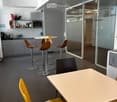 Modern break room with grey cabinets, a microwave, sink, and various seating options including stools and chairs around tables.