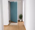 Empty hallway, white walls, wooden floor, circular ceiling lamp, blue door.