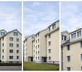 Apartment building with many windows, beige exterior, two entrances on the left, a grassy area in the middle