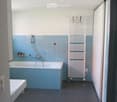 Modern bathroom with blue tiles, a bathtub, a showerhead, a white radiator, a small stool, and a grey rug on the floor.