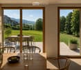 Bright kitchen with large sliding glass doors opening to a patio, wooden dining table with chairs, vase with greenery, bowl of fruit, and glassware.