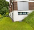 Modern two-story house with white and wood exterior, surrounded by a well-maintained lawn and trees.
