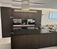 Modern kitchen with dark wood cabinets, black countertop, induction stove, oven, sink, and decorative items on the island.