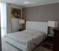 Modern bedroom with a large bed, white headboard, nightstands with lamps, and a painting on the wall.